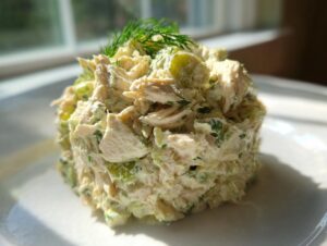 A perfectly molded serving of creamy dill pickle chicken salad garnished with fresh dill.