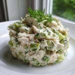 A scoop of creamy dill pickle chicken salad mixed with chunks of pickles and topped with fresh dill sprigs.