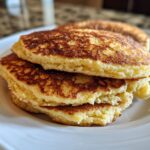 Close-up of a stack of three fluffy almond flour pancakes with golden-brown, perfectly seared tops.