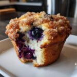 A close-up of a fluffy blueberry muffin with a bite taken out, revealing juicy berries and a sugary streusel topping.