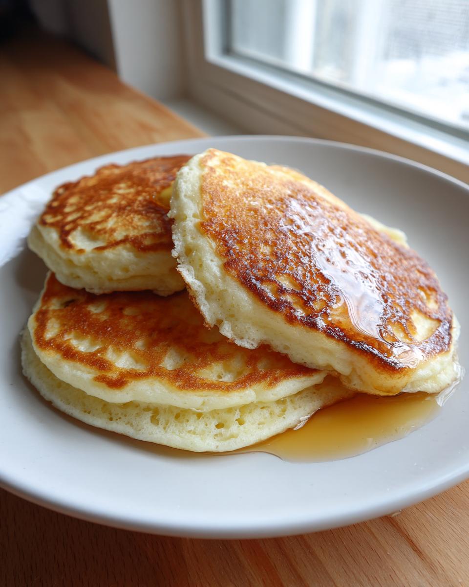 A stack of three fluffy discard pancakes drizzled with maple syrup on a white plate.