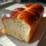 Close-up of a freshly baked japanese milk bread loaf, showing its incredibly soft, white crumb and shiny, golden-brown top.