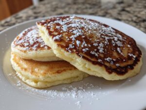Close-up of a stack of three fluffy sourdough discard pancakes dusted heavily with powdered sugar on a white plate.