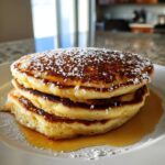 A stack of three fluffy sourdough discard pancakes drizzled with syrup and dusted with powdered sugar.