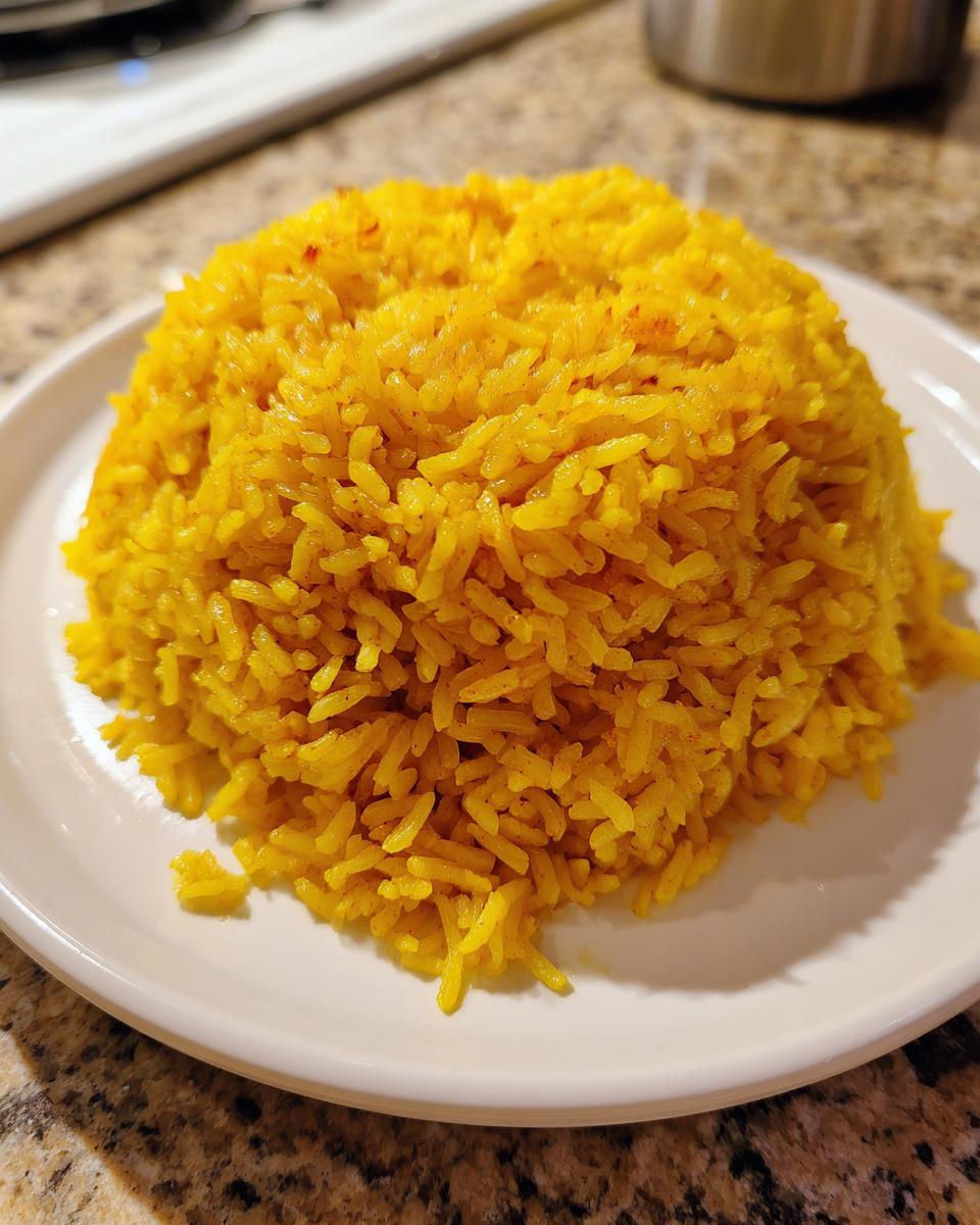 A mound of vibrant yellow turmeric rice served on a simple white plate, ready to eat.