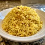 A close-up of fluffy, bright yellow turmeric rice mounded high in a white serving bowl.
