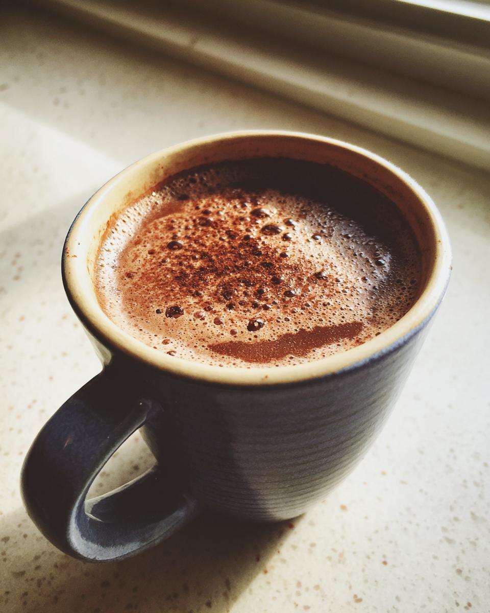 A close-up of rich, foamy mexican hot chocolate dusted with cinnamon in a dark blue mug.