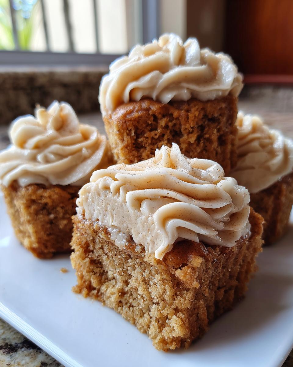 Close-up of several moist banana cupcakes topped with cinnamon-dusted cream cheese frosting, one cut in half.
