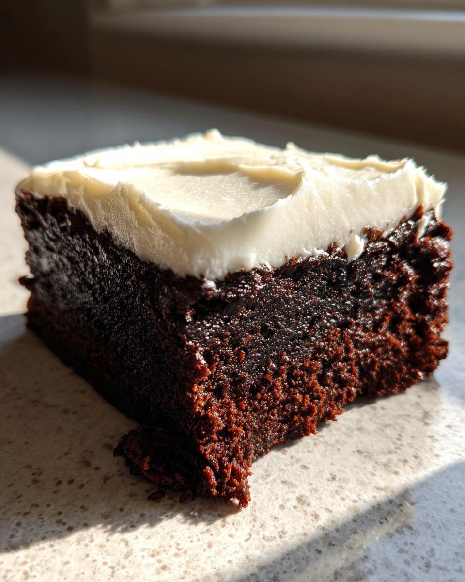 A close-up, sunlit shot of a rich, dark slice of gingerbread brownies topped with thick white cream cheese frosting.