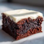 A single, rich, dark square of gingerbread brownies topped with thick, creamy white frosting.
