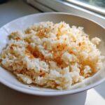 A close-up of fluffy white rice seasoned with butter and topped with crispy fried garlic, known as garlic butter rice.