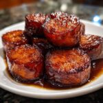 Close-up of thick-cut, perfectly glazed southern candied yams stacked on a white plate.