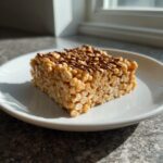 A single square of gooey peanut butter rice krispie treats drizzled with chocolate on a white plate.