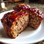 Close-up of a juicy mini meatloaf cut in half, showing the texture and topped with a thick, glossy glaze.