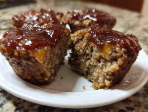 Close-up of a juicy mini meatloaf cut in half, showing the texture and thick glaze topping.