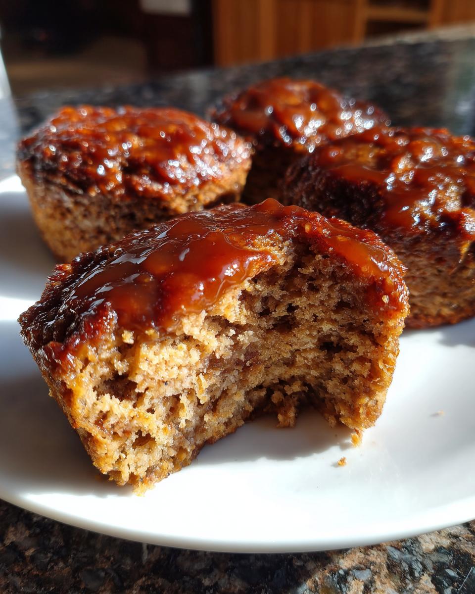 Close-up of a glazed mini meatloaf with a bite taken out, showing the moist interior texture.