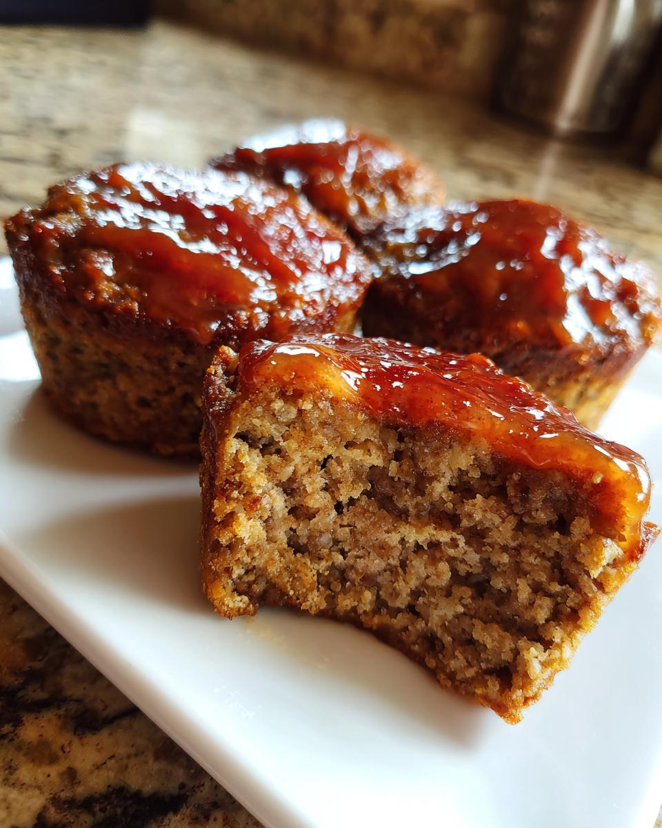 Close-up of a juicy mini meatloaf with a sweet glaze, showing the texture after a bite is taken.