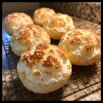 Six freshly baked, puffy keto cloud bread rolls cooling on a wire rack with a granite countertop background.