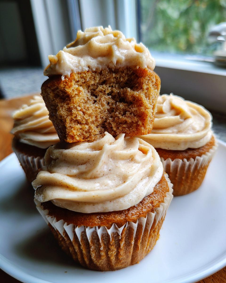 Three banana cupcakes on a white plate, one stacked on top showing the moist crumb texture inside.