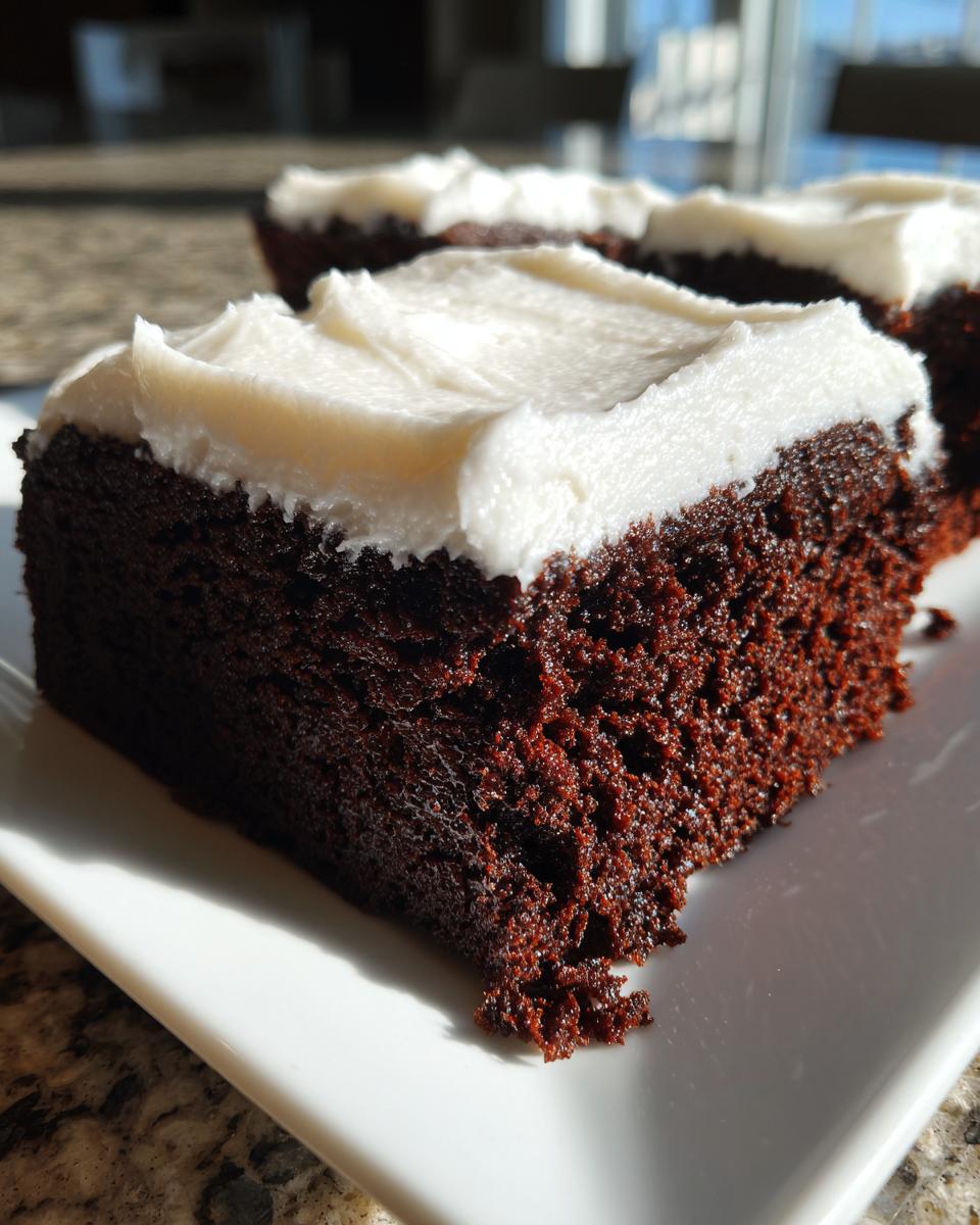 Close-up of a rich, dark slice of gingerbread brownies topped with thick white frosting.