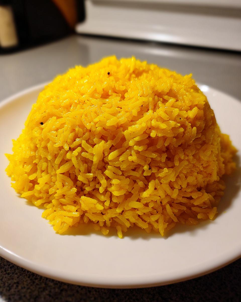 A perfectly molded mound of vibrant yellow turmeric rice served on a white plate.