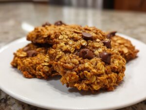 A stack of moist, oatmeal-based breakfast cookie treats topped with melted chocolate chips on a white plate.