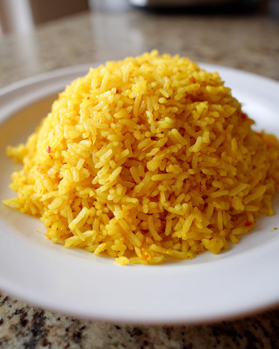 A close-up of a perfectly molded mound of bright yellow turmeric rice served on a white plate.
