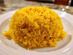 A close-up shot of a perfectly molded mound of bright yellow turmeric rice sprinkled with red chili flakes on a white plate.