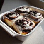 Four freshly baked Oreo cinnamon rolls covered in white icing and crushed chocolate cookies.