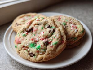 Three soft-baked peppermint chocolate chip cookies topped with crushed candy cane pieces on a white plate.