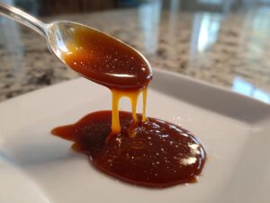 A spoonful of thick, glossy homemade caramel sauce is drizzled onto a white plate.