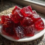 Close-up of sparkling, deep red chunks of homemade cinnamon rock candy piled on a small white plate.