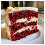 A tall, three-layer slice of vibrant red velvet cake layered and topped with thick white cream cheese frosting.