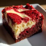 A rich, square portion of red velvet cheesecake brownies showing a vibrant red and cream cheese swirl.