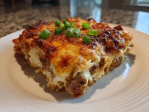A thick, golden-brown slice of baked pierogi casserole topped with melted cheese and fresh green onions.