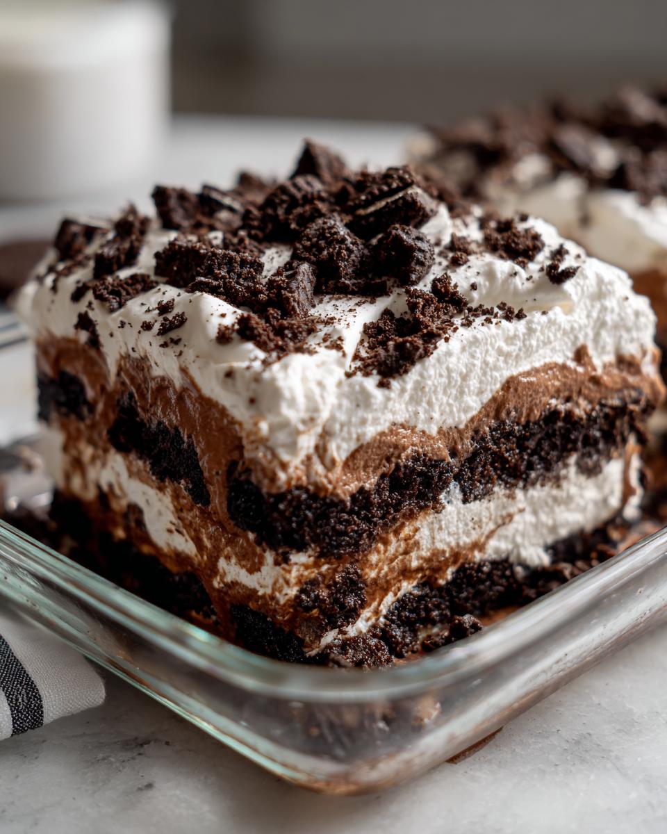 Close-up of a square serving of layered dirt cake featuring chocolate pudding, cream, and crushed Oreo cookies.