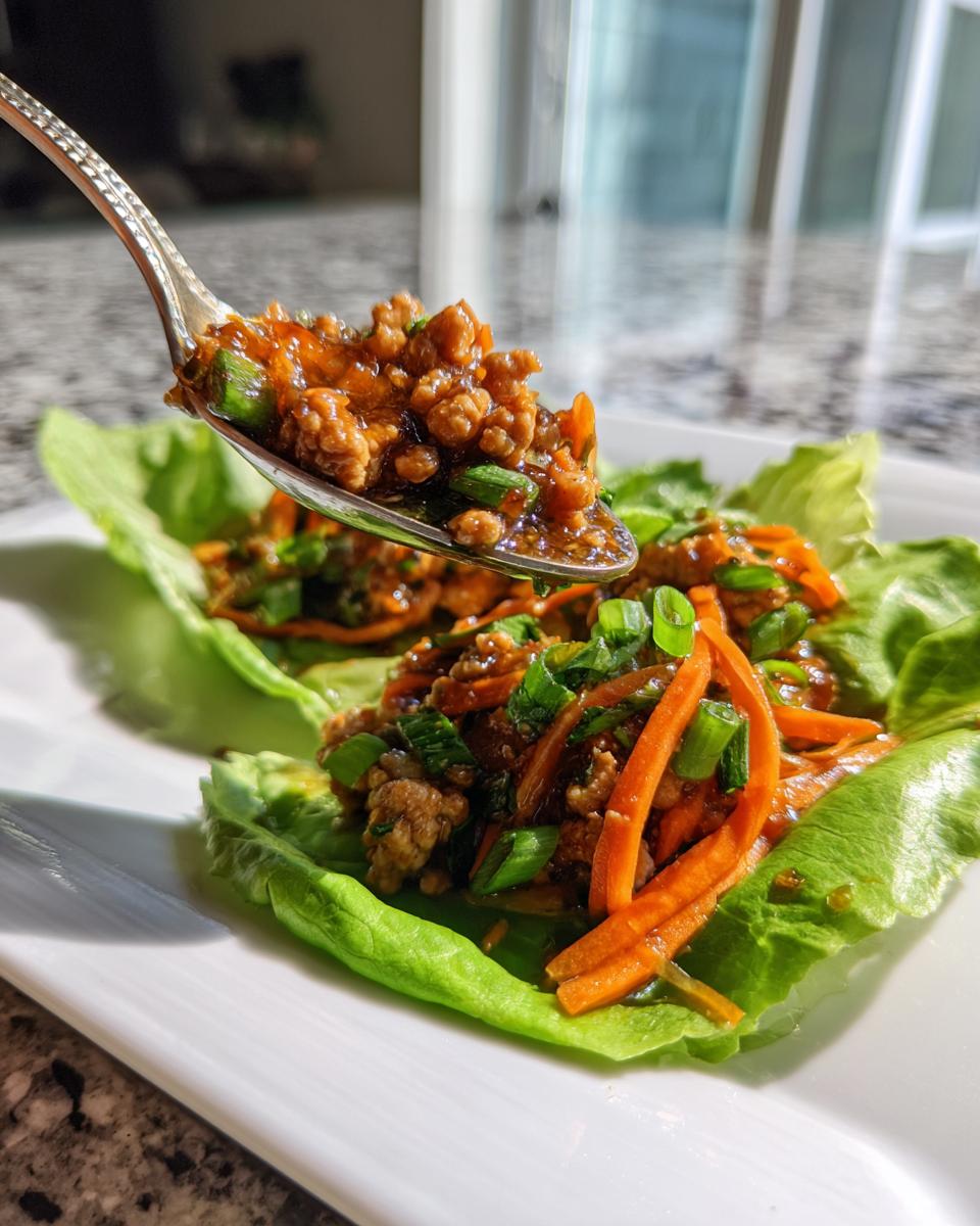 A spoonful of saucy ground chicken mixture being added to fresh thai chicken lettuce wraps.