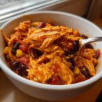 Close-up of shredded chicken in a bowl of slow cooker buffalo chicken chili with visible beans and corn.
