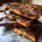 A stack of rich graham cracker toffee pieces topped with dark chocolate and sprinkled crumbs.
