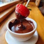 A fresh strawberry being dipped into a small white bowl of rich, melted chocolate fondue.