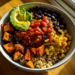 Close-up of a vibrant sweet potato taco bowl featuring roasted sweet potatoes, black beans, corn, salsa, and avocado slices.
