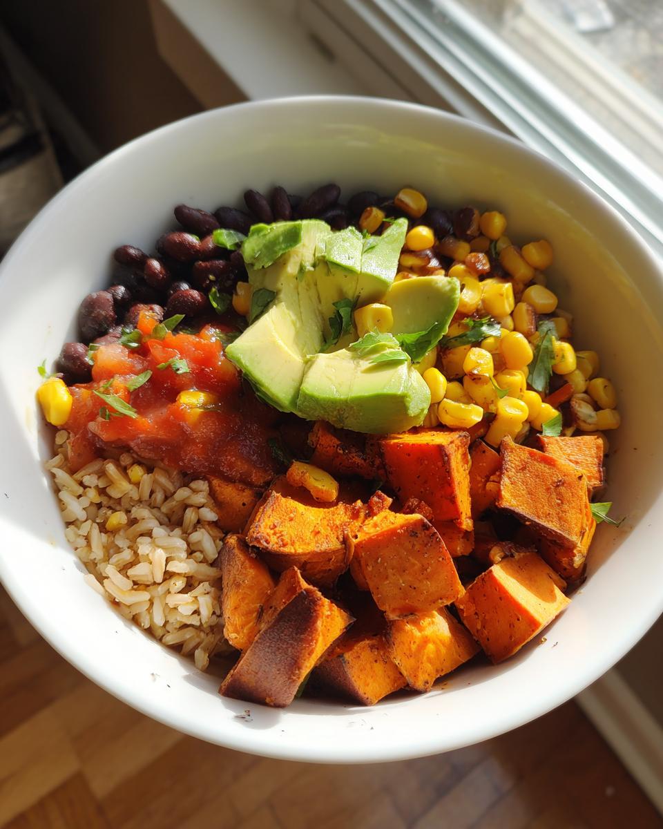 A vibrant sweet potato taco bowl featuring roasted sweet potatoes, brown rice, black beans, corn, salsa, and sliced avocado.