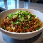 Close-up of a white bowl filled with savory egg roll in a bowl mixture, topped generously with fresh green onions and sesame seeds.