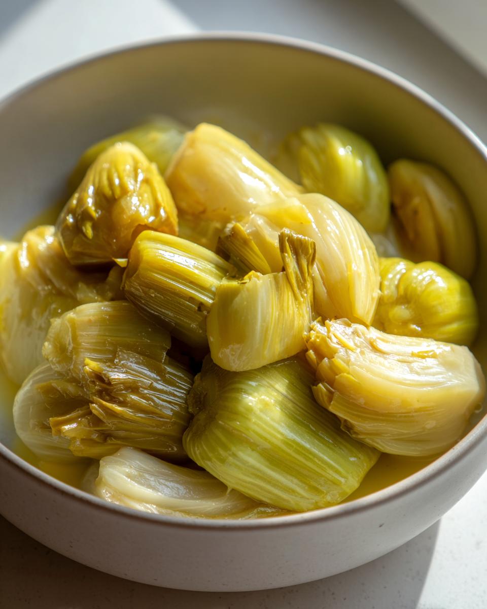 Close-up of tender, cooked braised leeks segments served in a light-colored bowl with cooking liquid.