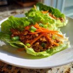 Close-up of prepared thai chicken lettuce wraps filled with savory ground chicken and topped with shredded carrots and scallions.