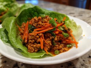 Close-up of savory ground chicken filling with shredded carrots served in a crisp lettuce cup for thai chicken lettuce wraps.