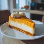 A perfect slice of two-layer pumpkin cheesecake showing a white cream cheese layer and an orange pumpkin layer, topped with whipped cream.