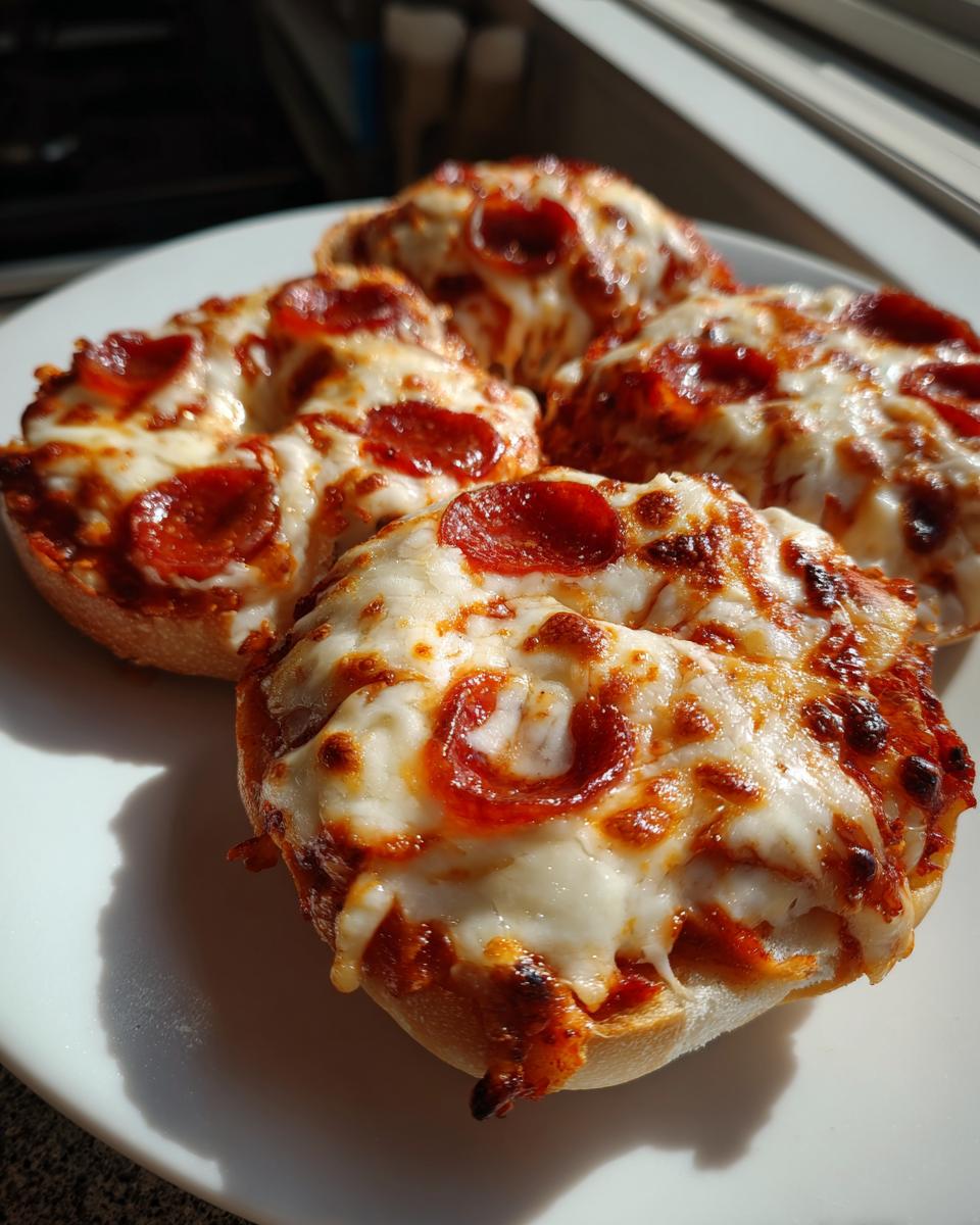 Four golden-brown pepperoni pizza bagels topped with melted, bubbly cheese served on a white plate.