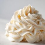 Close-up of a perfectly piped swirl of creamy, pale yellow vanilla buttercream frosting.
