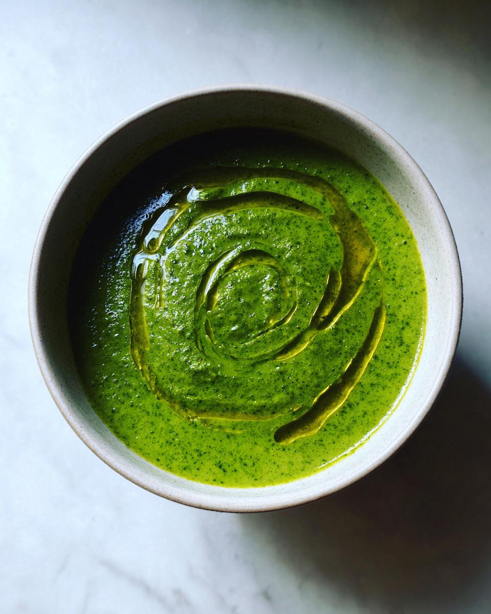 Overhead view of a bowl of bright green zucchini soup, drizzled with olive oil in a spiral pattern.
